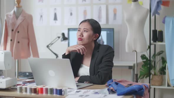 Asian Female Designer In Business Suit Working On A Laptop And Thinking While Designing Clothes 