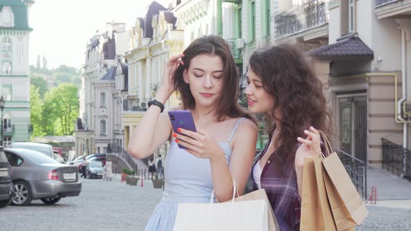 Two Young Female Friends Using Online Map on Smart Phone on City Streets