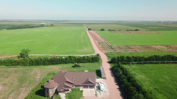 Aerial drone view following a gravel road out of a farm yard along a soybean field; farm equipment i