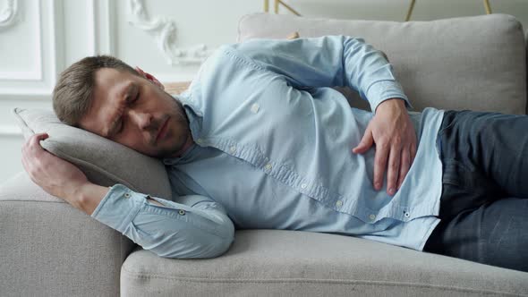 Man Suffering From Stomach Ache While Lying on Sofa at Home