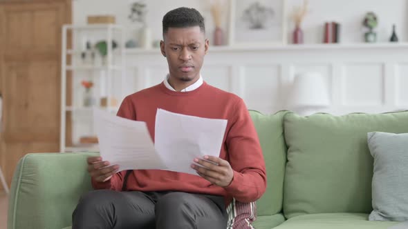 African Man Reacting to Loss on Documents, Sofa