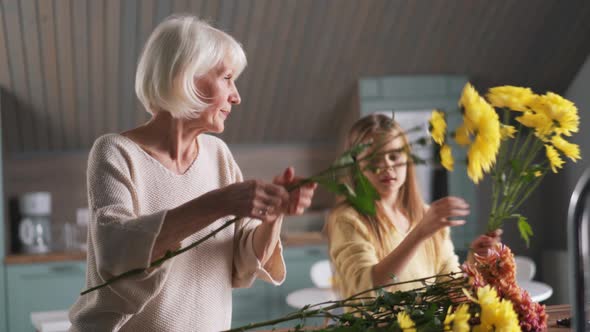 Happy girl helps to her grandmother collect a bouquet of flowers