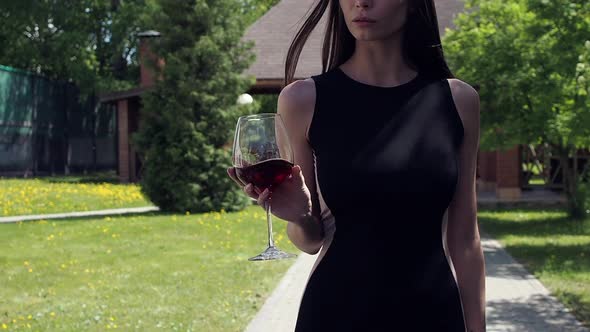 Elegant Woman with Glass of Wine Walking in Garden of Mansion