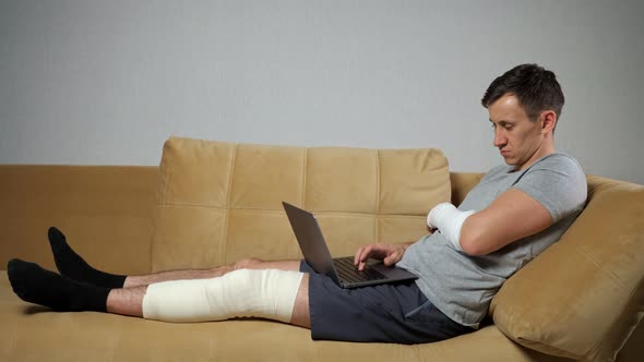 Man with Damaged Knee and Forearm Works Distantly Via Laptop