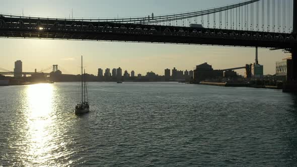 A  view over the East River at sunrise. The drone camera pan left and dolly in behind a sailboat by