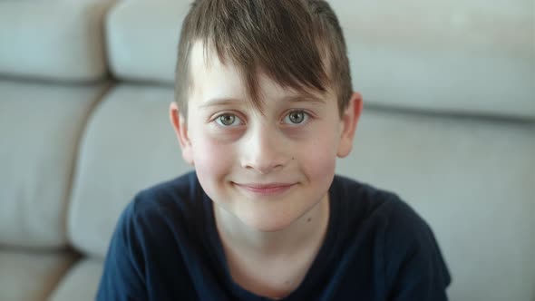 Portrait of cute 8 years old boy looking at camera and sitting on sofa at home