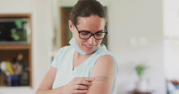 Caucasian woman wearing face mask pointing at bandage on her arm