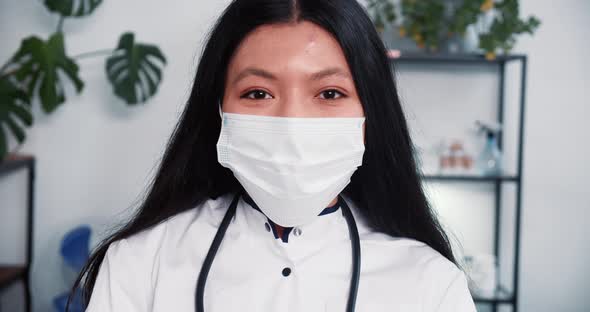 Closeup Young Happy Mixed Race Female Doctor Wearing Face Mask Lab Coat Smiles at Camera at Light