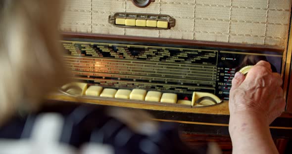 a Rear View of a Grayhaired Old Woman Who is Looking for a Radio Wave on a Vintage Radio with a