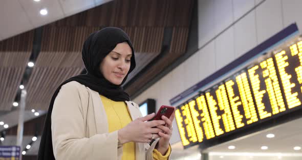 Smiling woman wearing hijab using smartphone at station