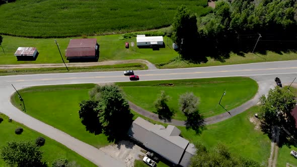 Aerial view of country road with cars commuting with cornfields and trees surrounding on a nice sunn