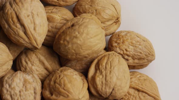 Cinematic, rotating shot of walnuts in their shells on a white surface