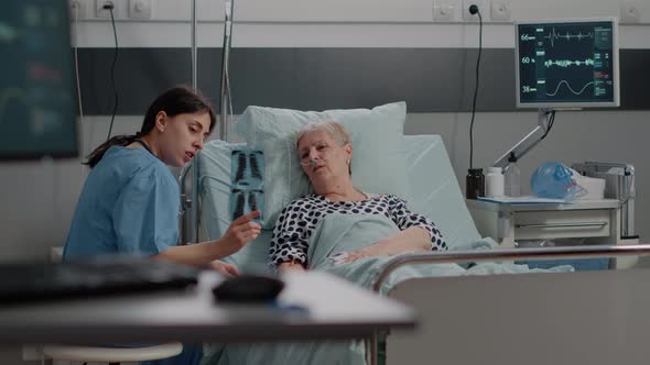 Medical Assistant Pointing at x Ray Scan for Senior Woman with Illness