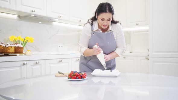 a Female Chef Adds Jam From a Pastry Bag to Anna Pavlova Cakes in the Kitchen