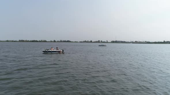 Drone Slomo of Small Boat on River with Male Friends Swimming and hanging on the boat, with passing