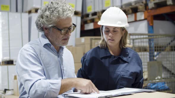 Focused Inspector and Female Worker Talking in Warehouse
