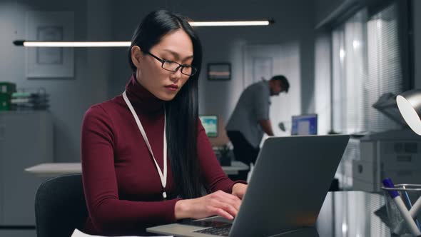 Young Asian Businesswoman Typing on Laptop in Modern Office