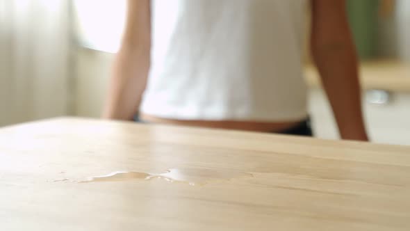 Housewife Wiping Spilled Coffee or Tea From a Wooden Kitchen Table. Female Using a Household Cleaner