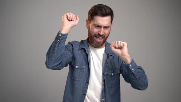 Im happy. Photo of handsome young bearded man dancing isolated over grey wall background.