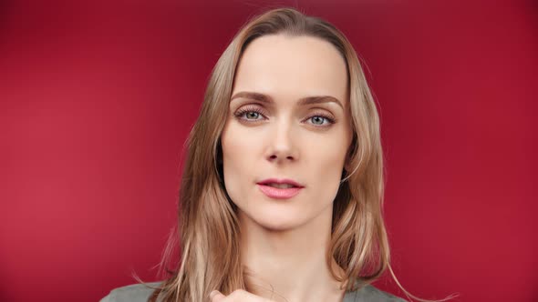 Face of Beautiful Young Blonde Woman Showing Silence Gesture Posing at Red Studio Background