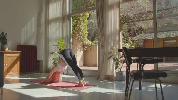 Beautiful Fit Blond Girl in a White Sports Short Top and Black Leggings Practicing Yoga at Home on a