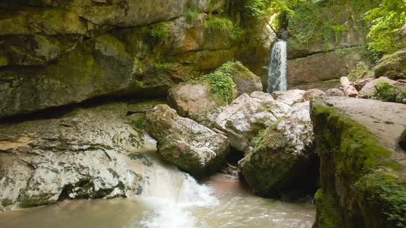 a Drone Flies Over a Mountain River Through Huge Rocks to a Waterfall