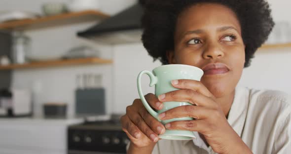 Happy african american woman drinking coffee in kitchen