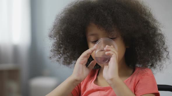 Thirsty Afro-American Kid Drinking Still Mineral Water, Close-Up of Child's Face