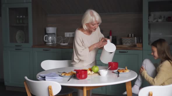 Positive grandmother pouring tea for granddaughter