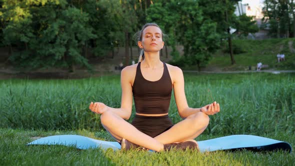 Beautiful Female Practicing Yoga in Lotus Position Outdoors in Sunny Day