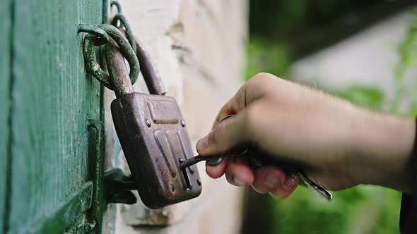 Closeup of a Caucasian Man's Hand Opens Old Padlock on the Green Wooden Door