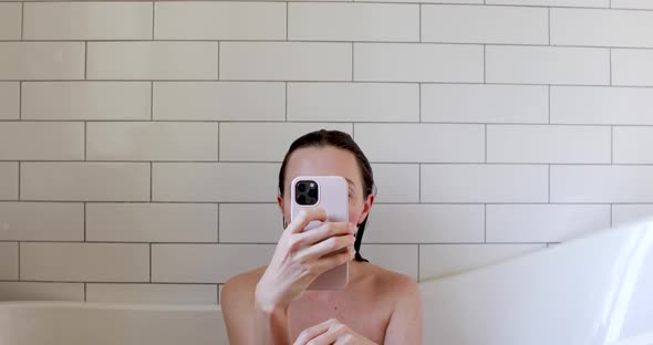 Bare Young Woman Holds Brown Smartphone Sitting in Bath