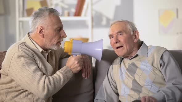 Elderly Male Talking in Megaphone to Deaf Old Friend, Health Problems, Close-Up