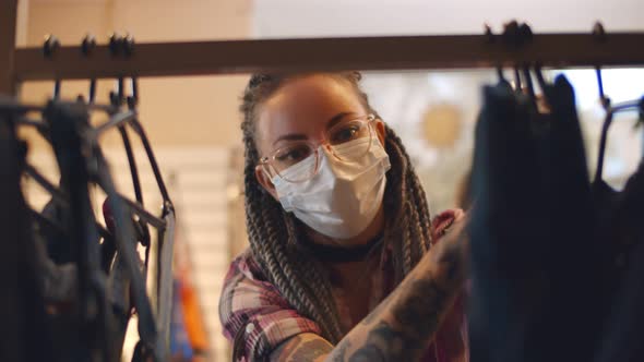 Young Woman Wearing Safety Mask Choosing Clothes in Rack in Shop