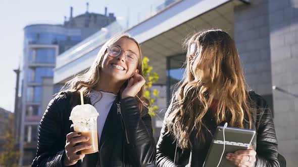 Two Young Caucasian Women Using Digital Tablet and Smiling Happily while Walking in City