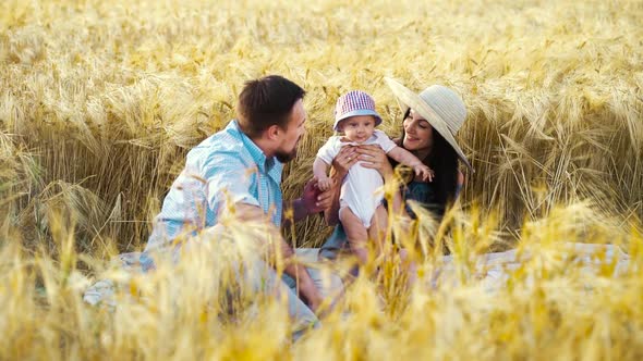 Happy family with sweet baby sitting in wheat field in summer