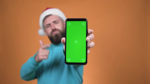 A man holds a phone with a green screen in front of the camera