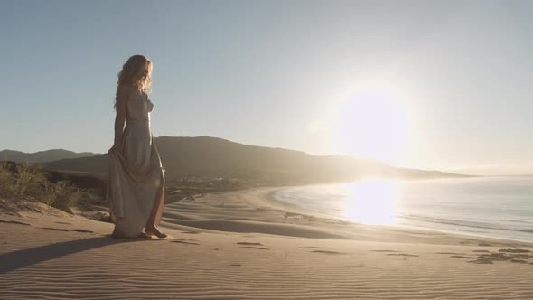 Blond Woman In Flowing Dress Walking On Beach