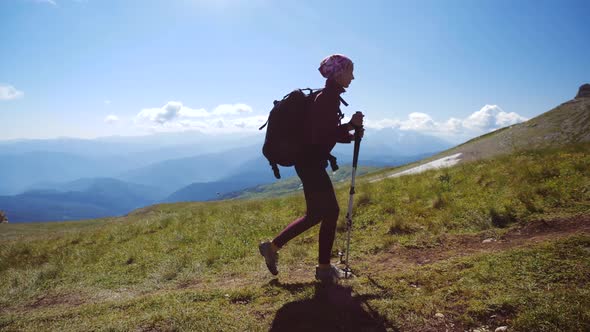 Young Woman with Backpack and Trekking Poles Walks Uphill Towards the Summit. Slow Motion. Lady Is