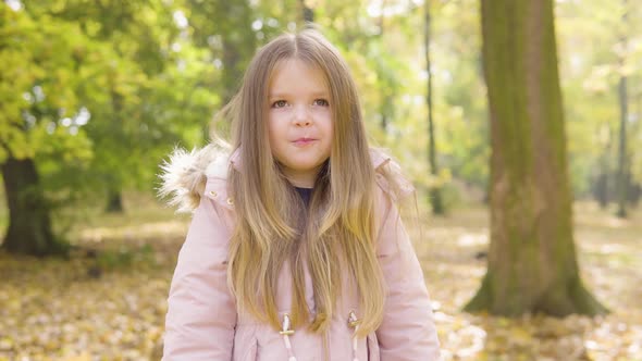 Cute Little Caucasian Girl Thinks About Something and Eats in a Park