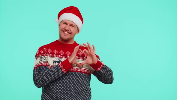 Smiling Man in Christmas Sweater Makes Heart Gesture Demonstrates Love Sign Expresses Good Feelings