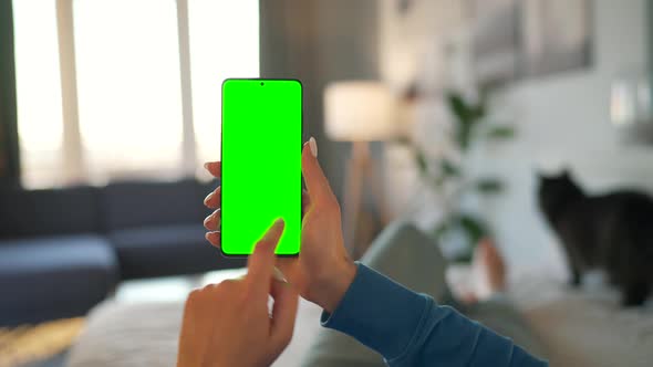 Woman at Home Lying on a Bed with Black Cat and Using Smartphone with Green Mockup Screen in