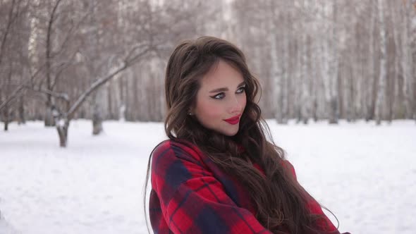 Young Woman with Wavy Hair Standing and Touching Face in Winter Forest