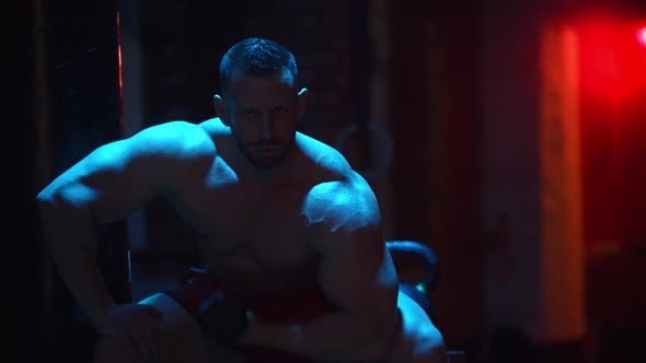 Strong Man Pumping His Biceps in Contrast Lighting and Looking in the Camera