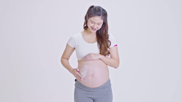 Asian Pregnant Woman standing on white background stroking apply cream on big belly