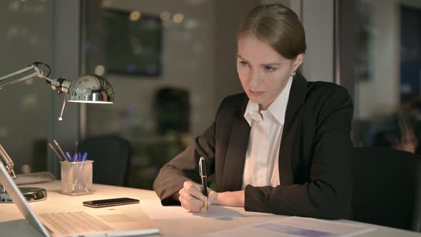 Focused Businesswoman Thinking and Writing on Document at Night 