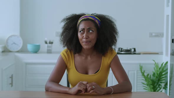 A Young Perplexed Multiethnic Woman Sitting at the Wooden Table in the Kitchen of a New Apartment