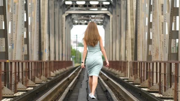 Back View of a Slim Woman with Long Hair Walking Along Train Tracks