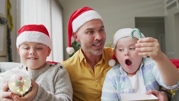 Portrait of caucasian father and two sons holding a snow globe and candy cane sitting on couch