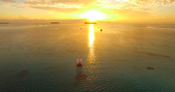 Aerial drone view of a man and woman having dinner on a floating raft boat at sunset.